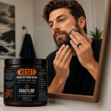 Man applying beard softening cream in front of a mirror with a jar of Coastline Skincare Reset Cream on a surface.